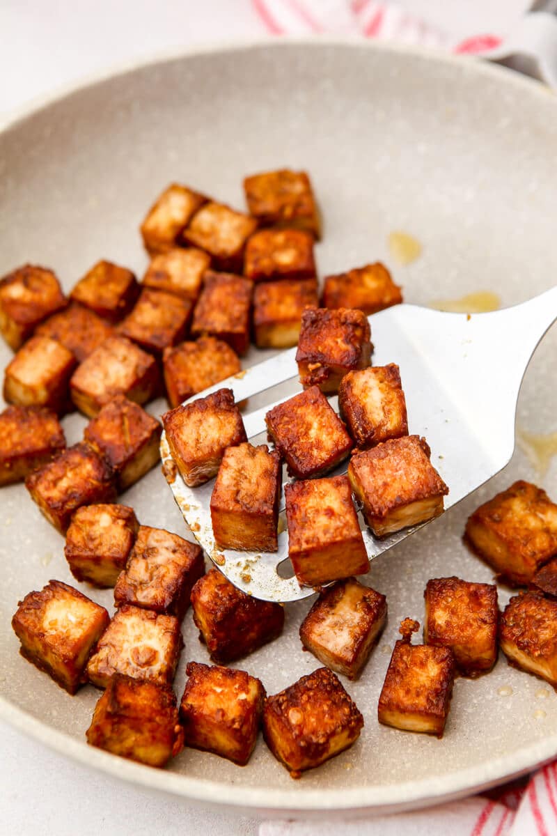 Marinated tofu being pan fried in a white skillet.