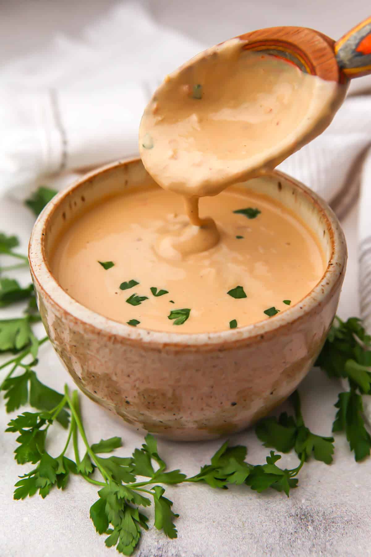 A bowl full of spicy tahini sauce with parsley around it.