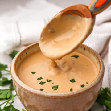 Spicy tahini sauce in a bowl with a colorful wooden spoon scooping some out.