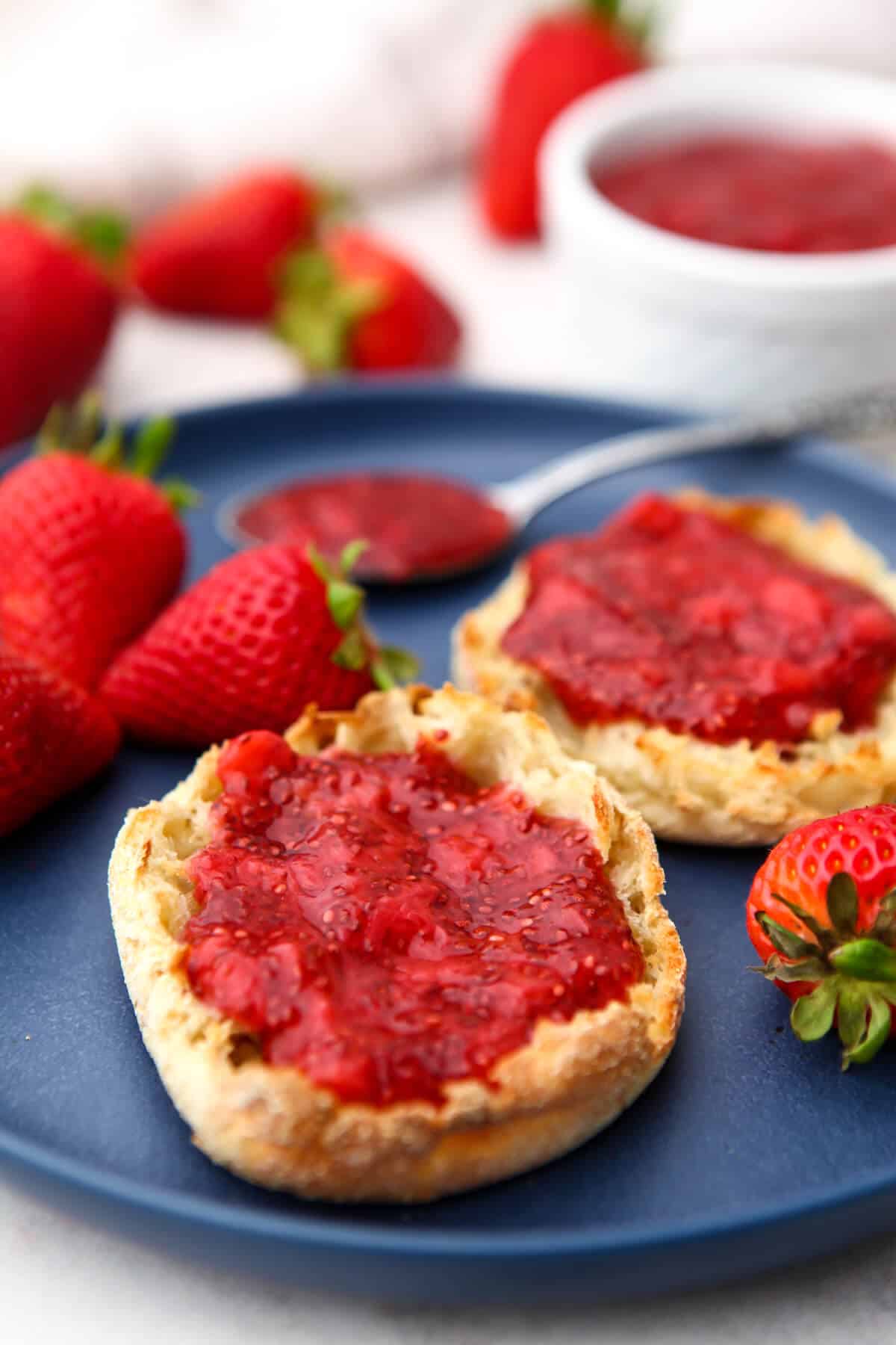 Vegan strawberry chia jam spread on English muffins sitting on a blue plate.