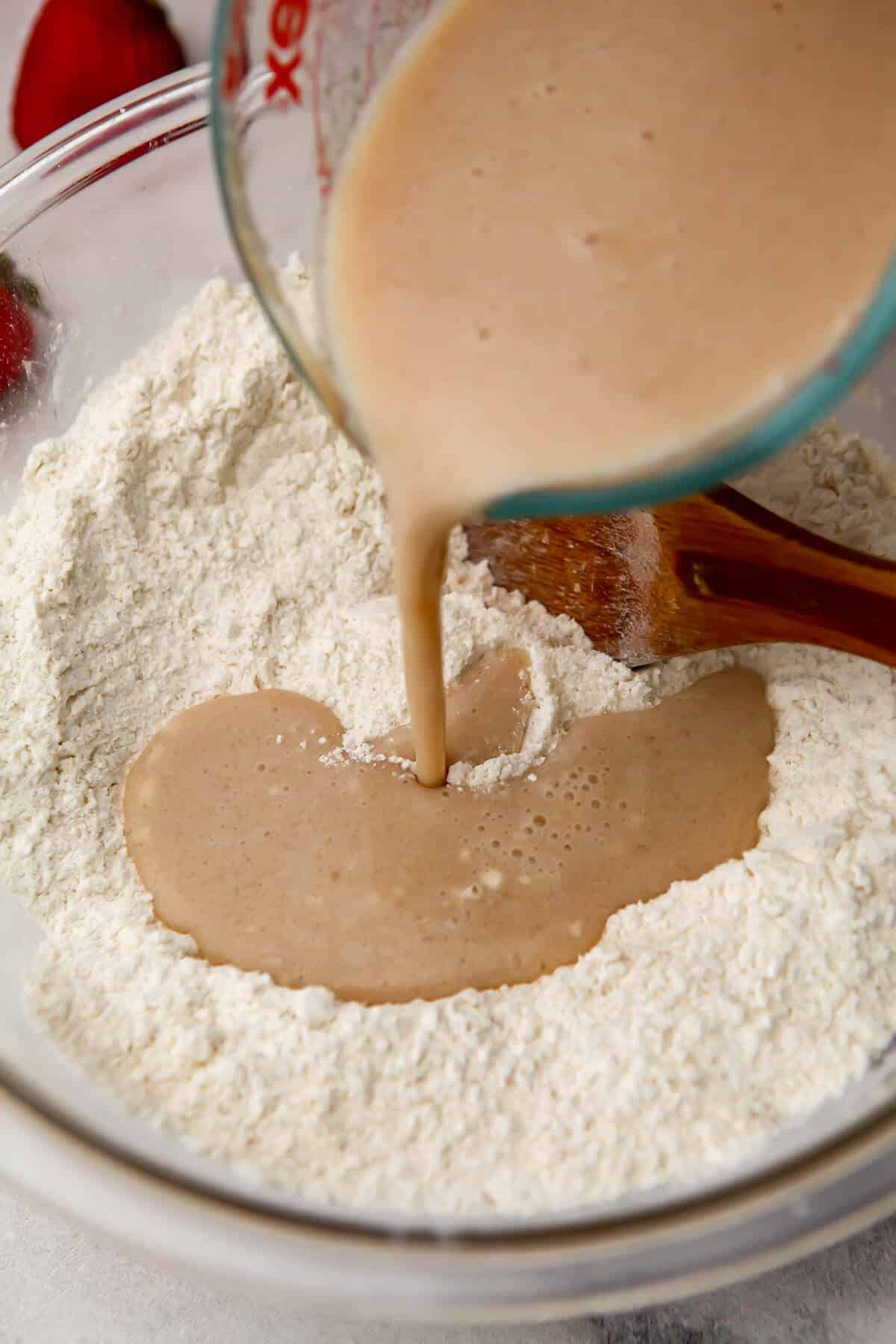 Pour the wet ingredients into the dry ingredients to make strawberry muffins.