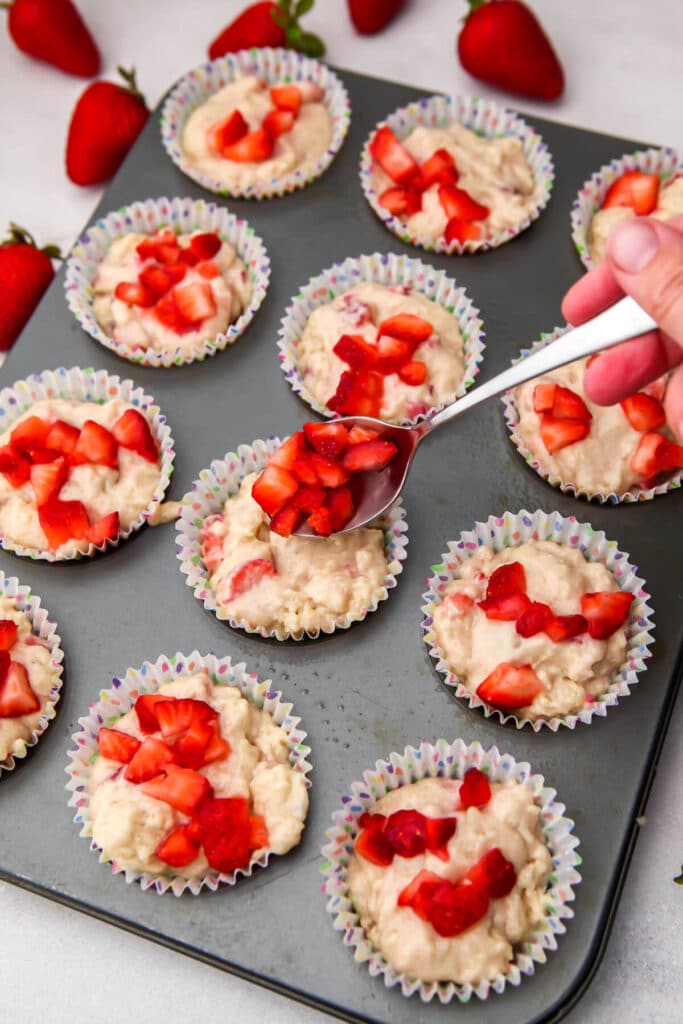 Topping muffins with fresh strawberries before baking.