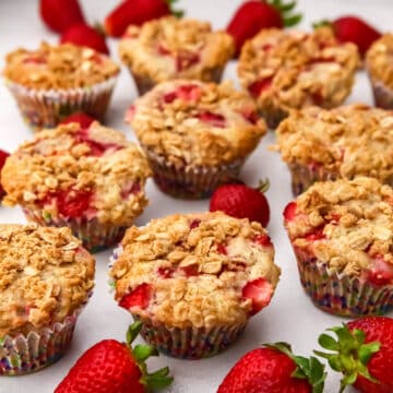 Vegan strawberry muffins cooling on a countertop with fresh strawberries around them.