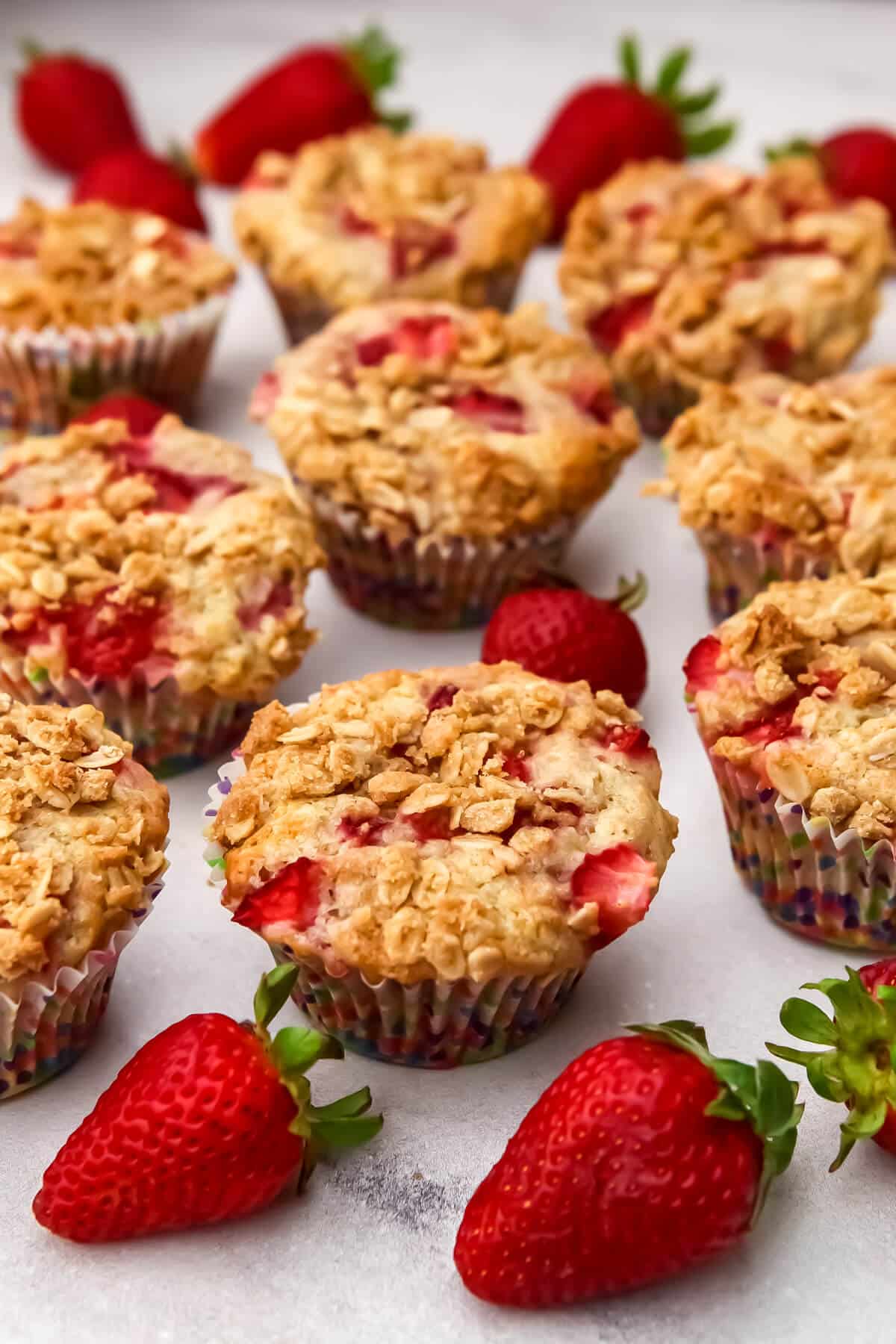 Vegan strawberry muffins on a countertop with strawberries around them.