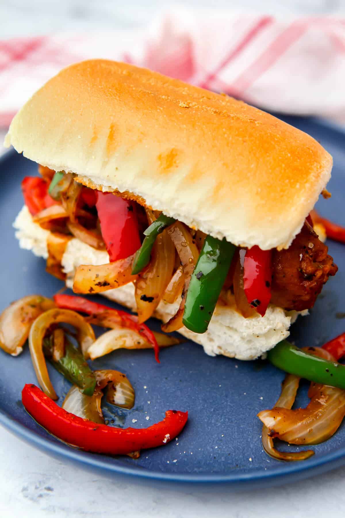 A vegan sausage and pepper sandwich on a blue plate.