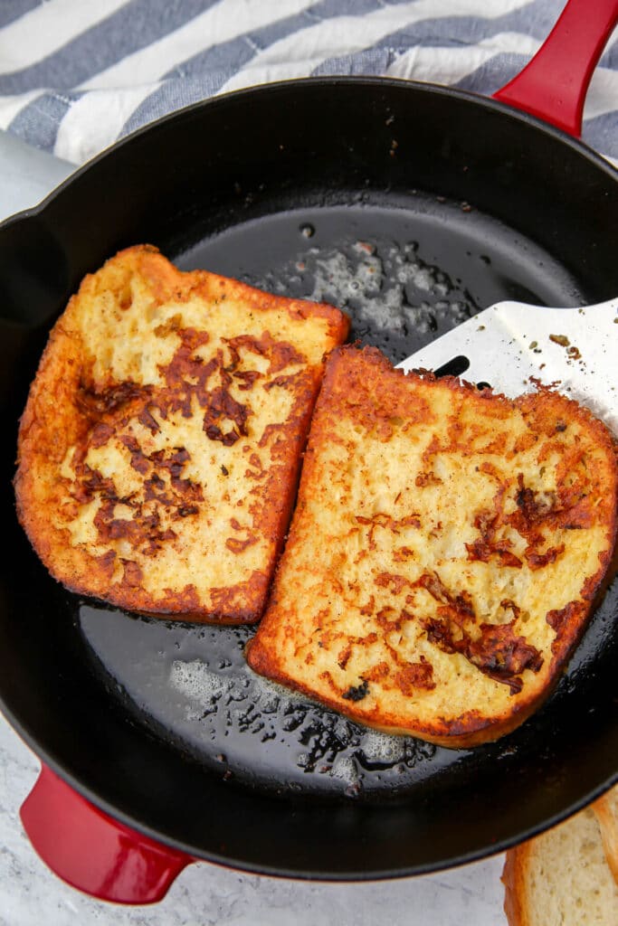 Two slices of vegan French toast cooked in an iron skillet with a red handle.