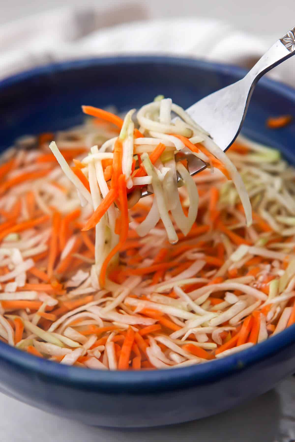 A blue bowl filled with bahn mi veggies being stirred with a fork.