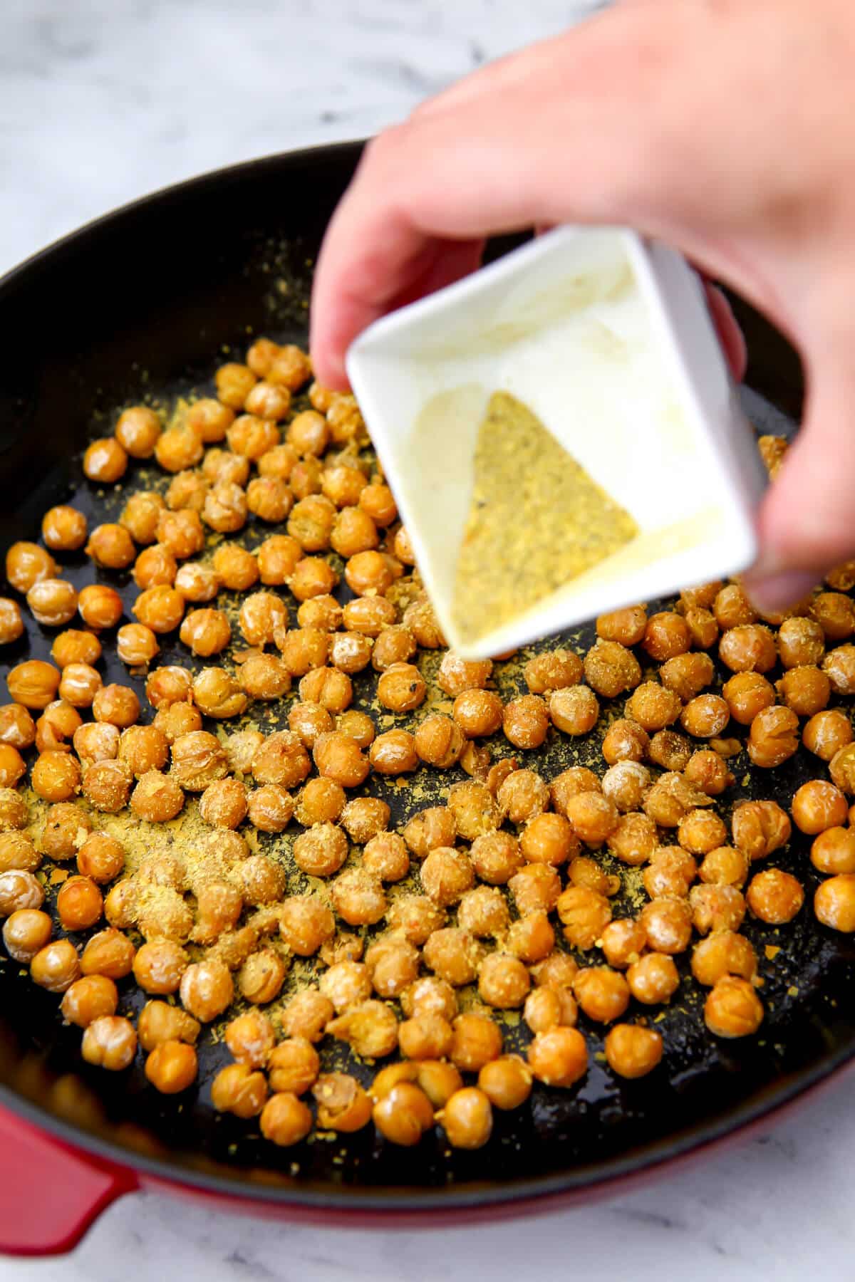 Sprinkling the sauteed chickpeas with seasoning after cooking.