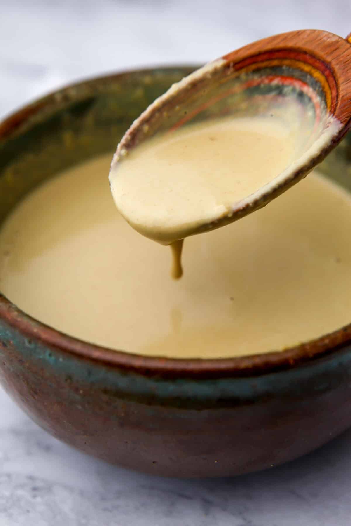 Tahini Caesar dressing after water has been added mixed in a bowl and dripping off a spoon.