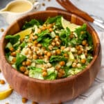 A wooden bowl filled with salad with vegan tahini Caesar dressing and chickpea croutons.
