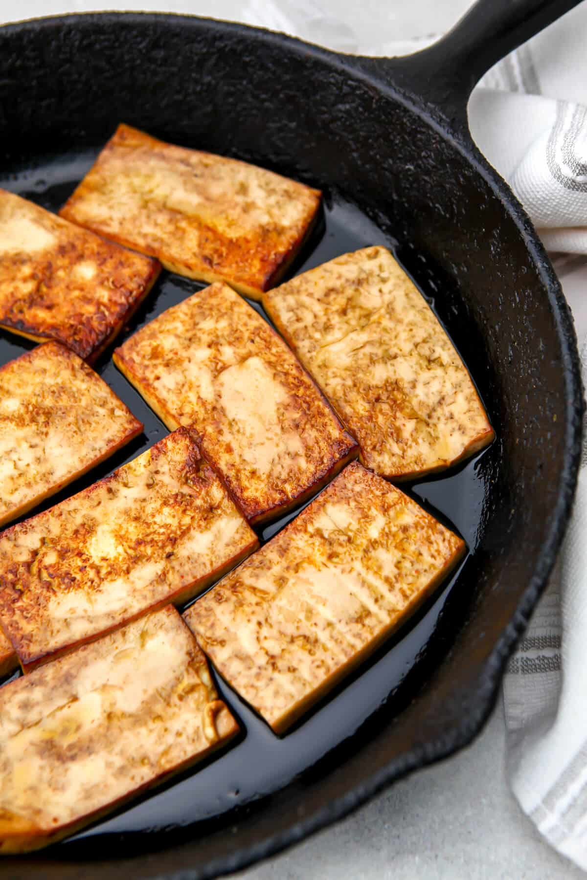 Sliced marinated tofu cooking in an iron skillet.