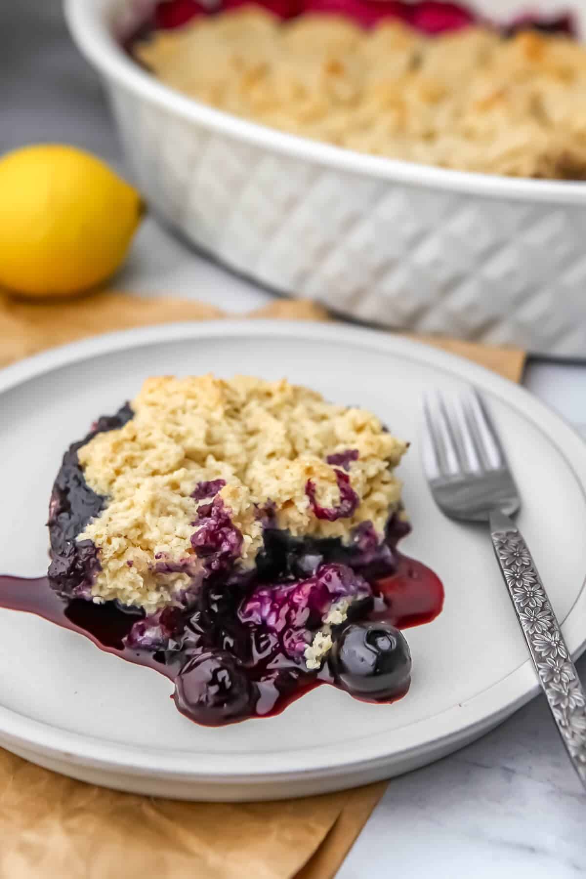 A white plate with a serving of vegan blueberry cobbler with a fork on the side.