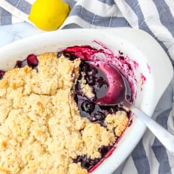 A vegan blueberry cobbler in a white baking dish with a scoop taken out of it.