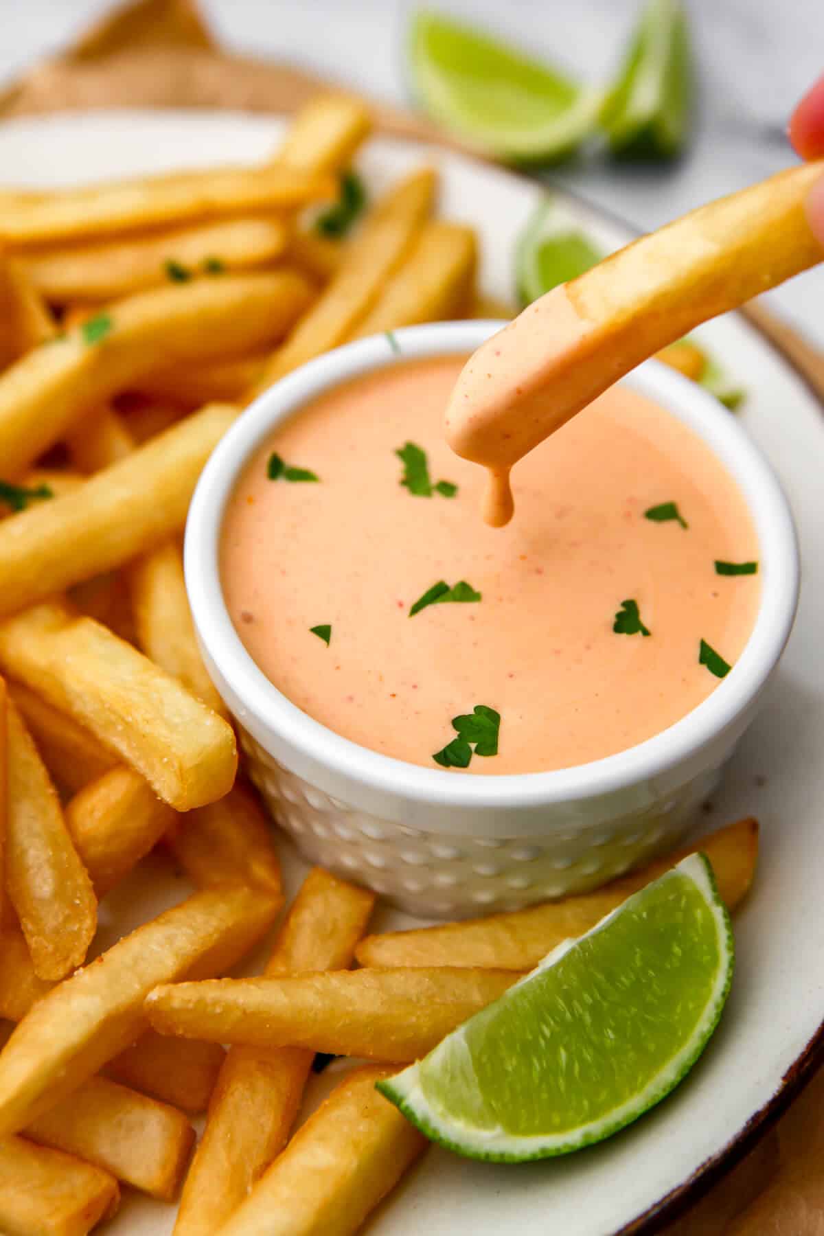 A french fry being dipped into a small bowl of vegan sriracha mayo.