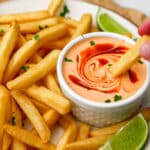 French fries on a white plate being dipped into a small white bowl of vegan sriracha mayo.