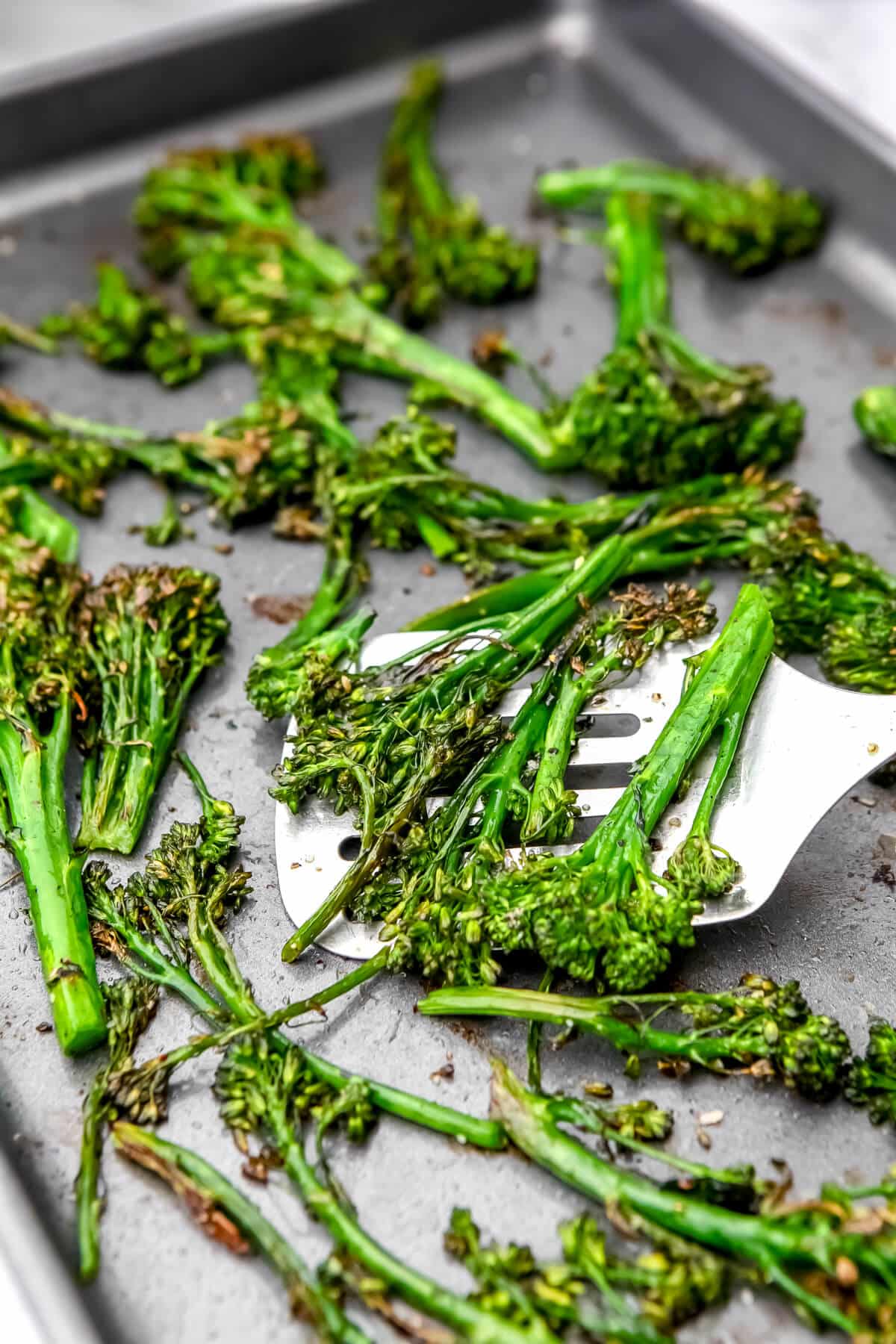 Oven roasted broccolini being flipped with a spatula.