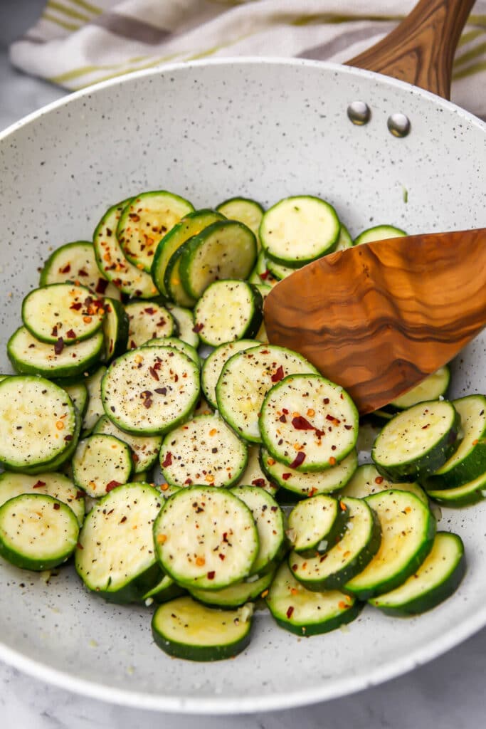 Sliced zucchini with garlic, salt, and spices in a large skillet.