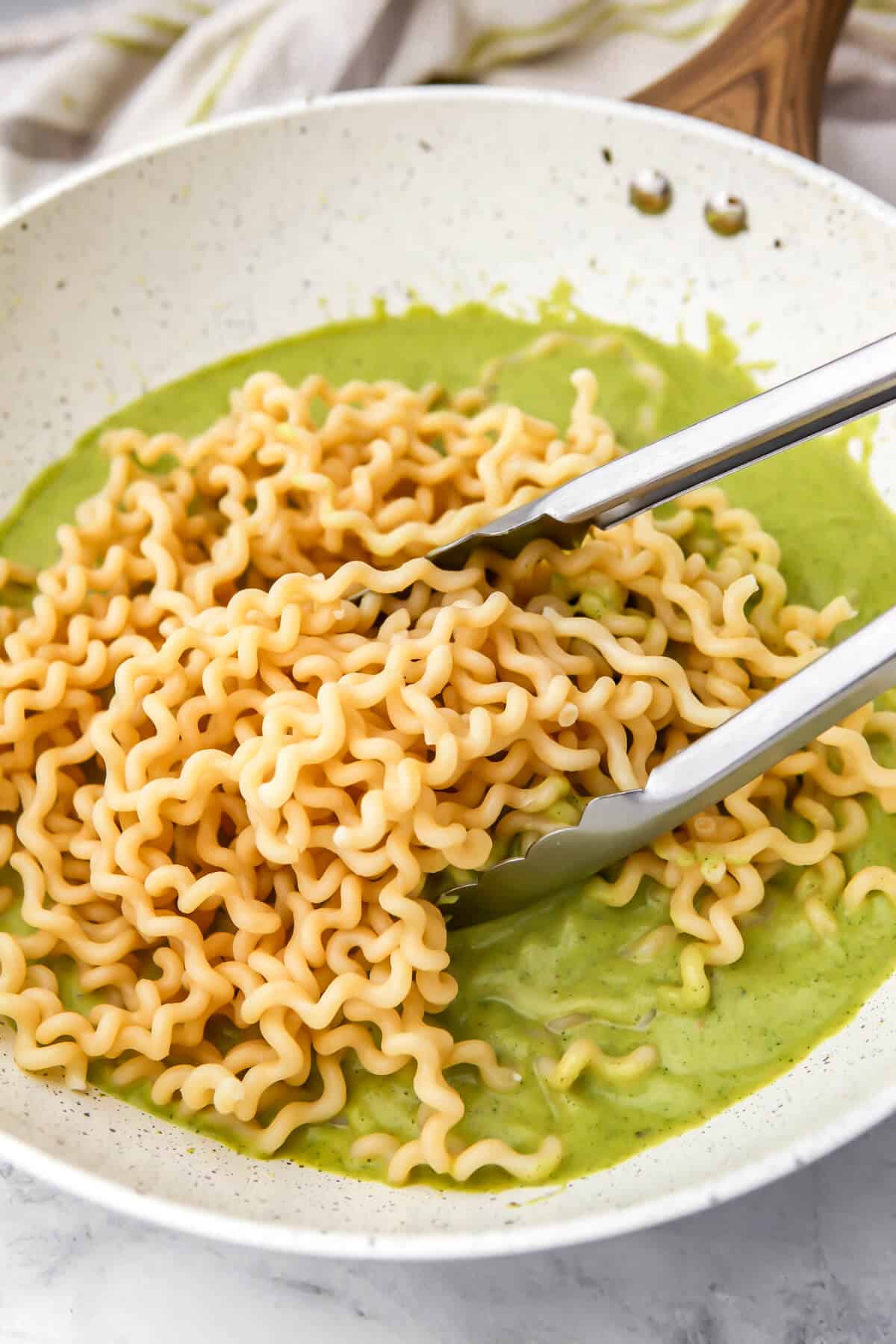 Mixing zucchini pasta sauce with the pasta.