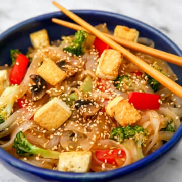Pad woon sen with tofu in a blue bowl with chopsticks on the side.