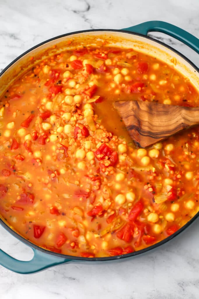 Chickpea, red lentils, tomatoes, and broth added to a skillet to make curry.