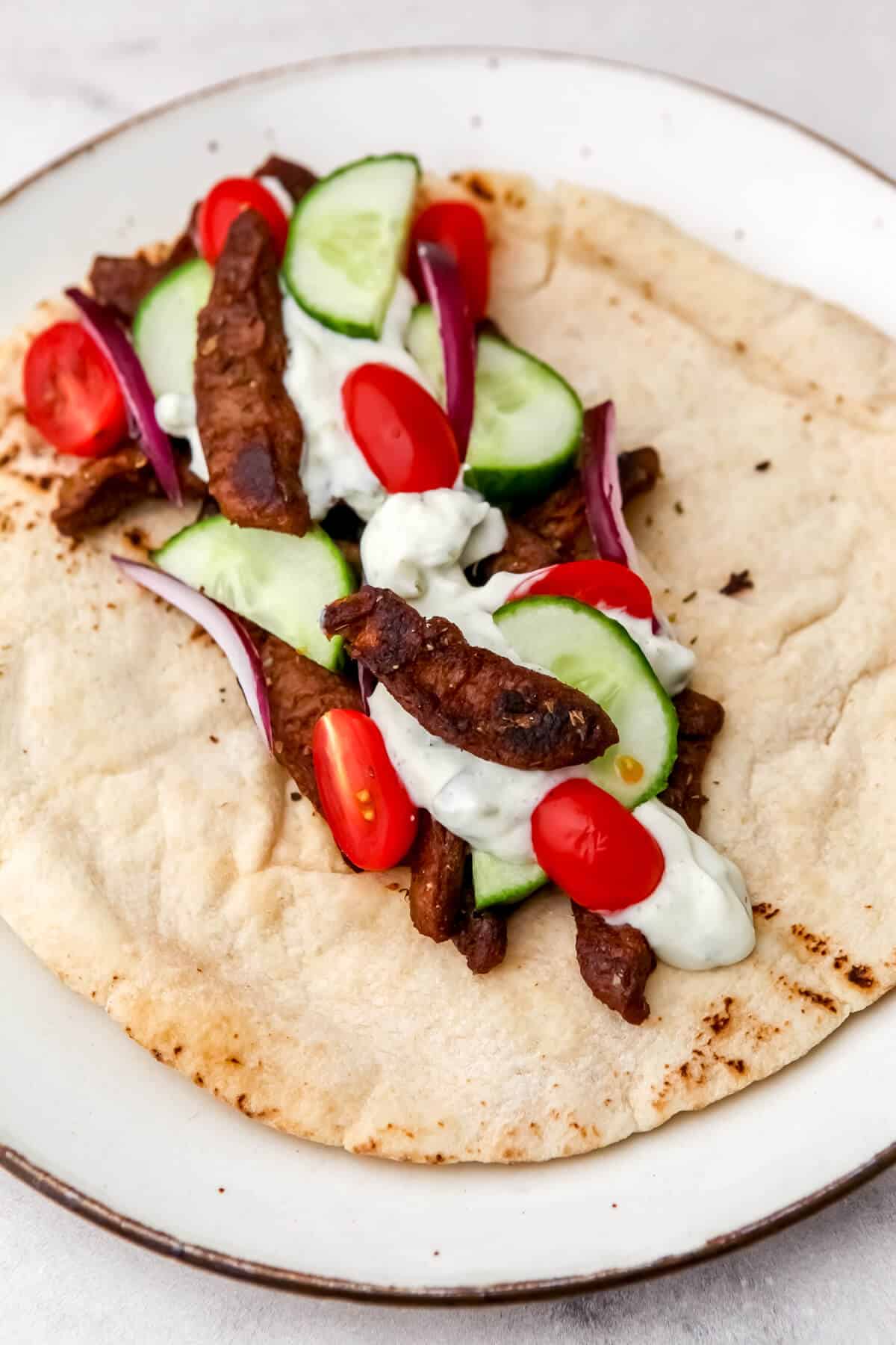 Vegan seitan, cucumber slices, cherry tomatoes, and vegan tzatziki on a pita before rolling into a wrap.