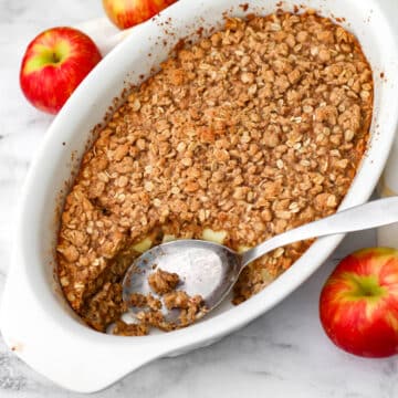 A white casserole dish with vegan baked oats with apples in it with more apples around it.
