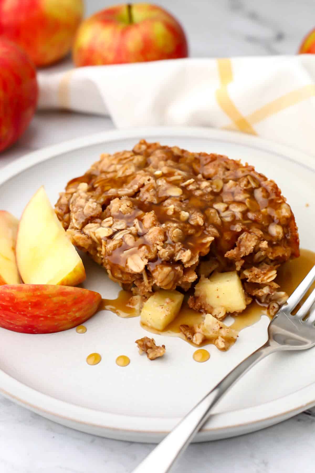 Vegan baked oats on a plate with slice apples on the side and caramel poured over it.
