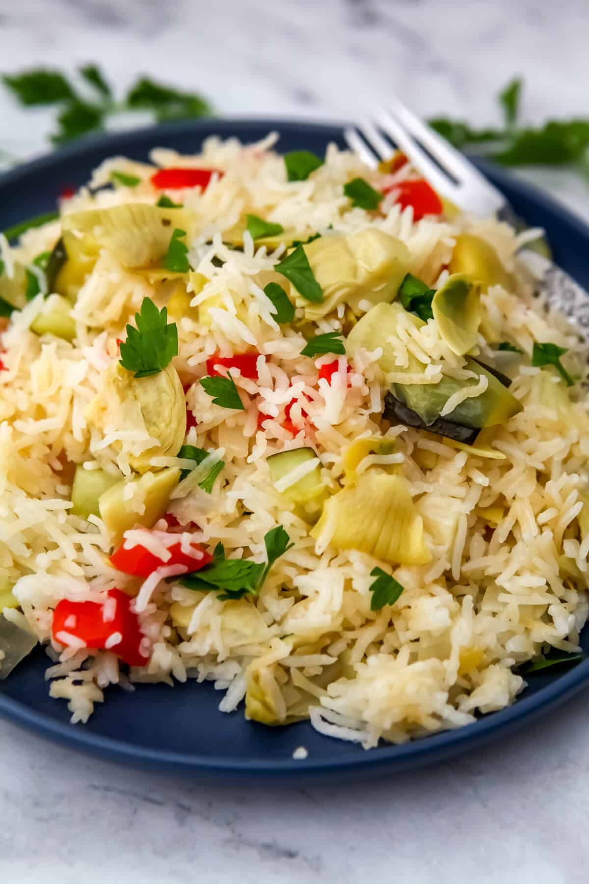 A blue plate full of vegan rice pilaf made with onions, peppers, and artichoke hearts topped with lemon juice and parsley.