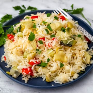 A plate full of vegan rice pilaf made with onions, red bell peppers and artichoke hearts with parsley on top and on the side.