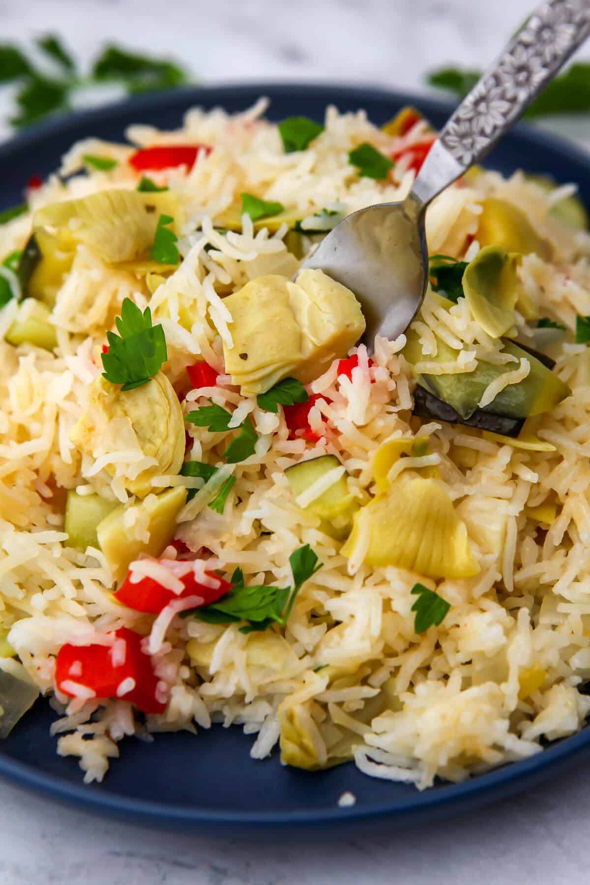 A blue plate filled with vegan rice pilaf made with onions, zucchini, bell pepper, and artichokes.