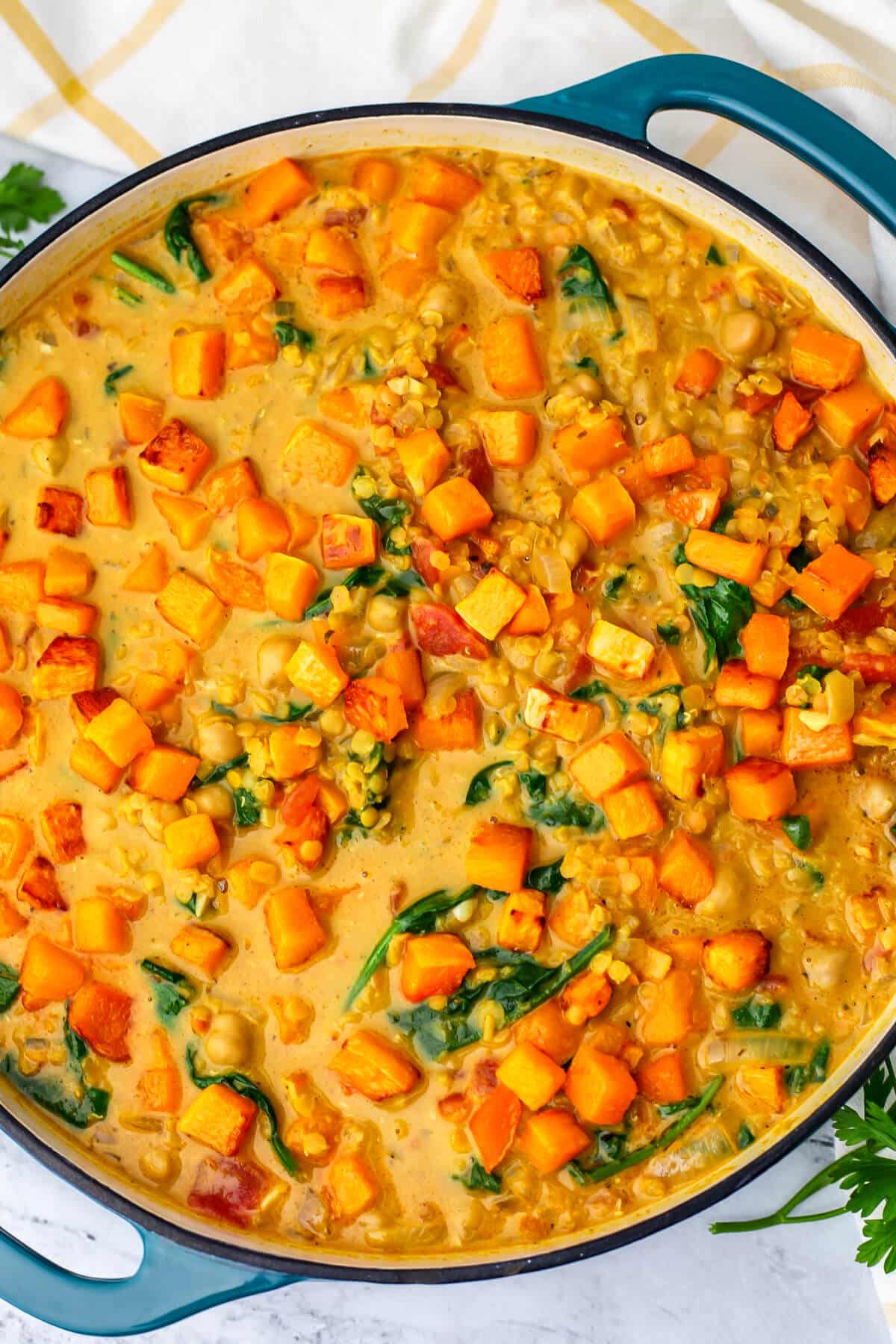 A top view of a pot of roasted squash curry with red lentils, chickpeas and spinach.