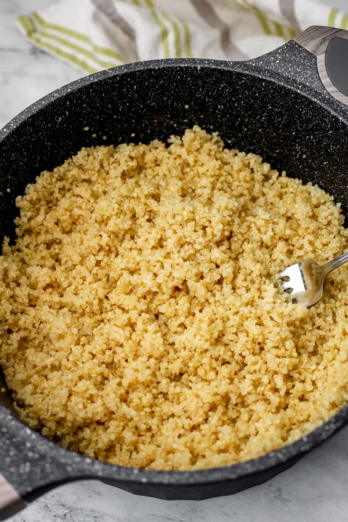 A pot of quinoa being fluffed with a fork.