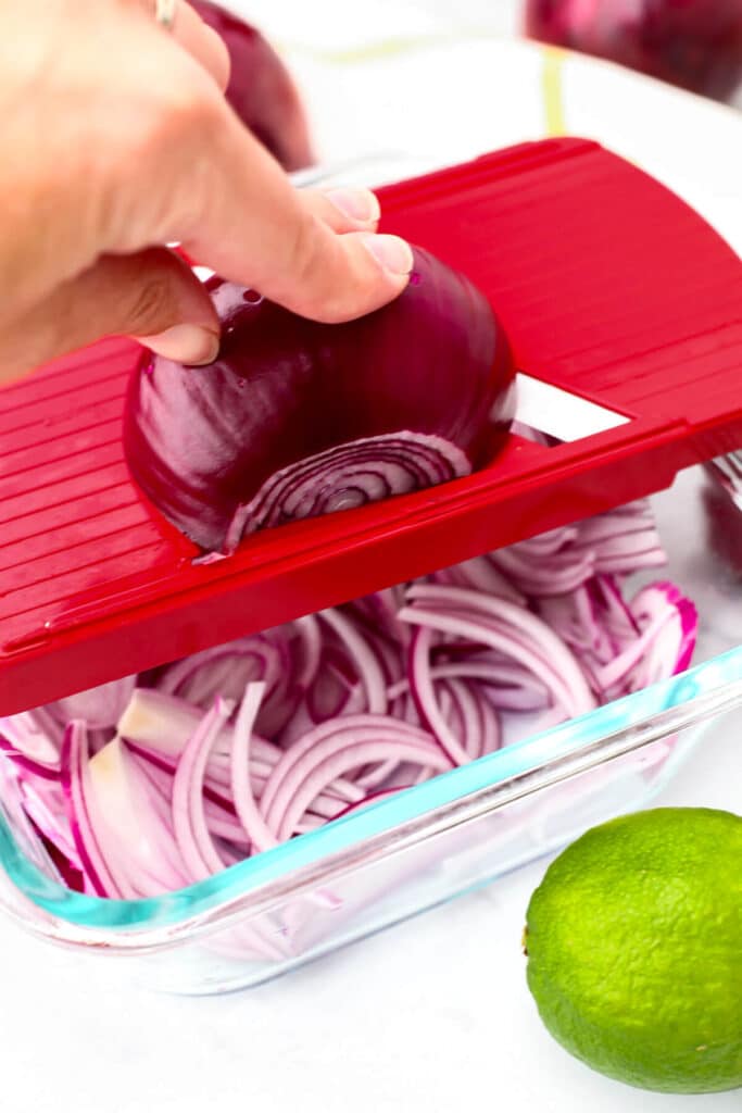 Slicing red onions with a red mandoline slicer.