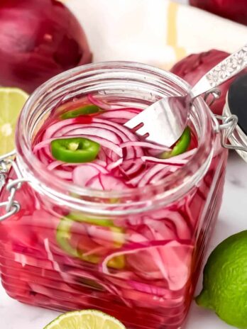 A glass jar full of Mexican pickled red onions and jalapenos with a fork in it.