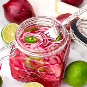 A glass jar full of Mexican pickled red onions and jalapenos with a fork in it.