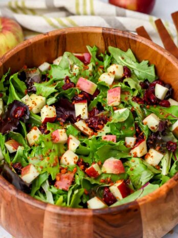 A green salad in a wooden bowl with diced apples and maple dressing on top.
