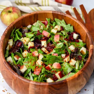 A green salad in a wooden bowl with diced apples and maple dressing on top.