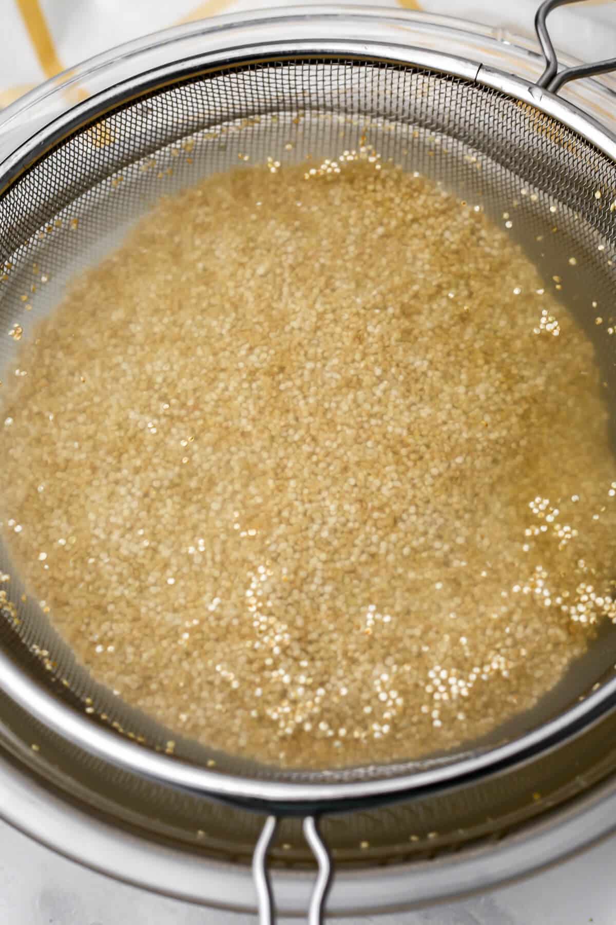 Soaking uncooked quinoa in a bowl of cold water before rinsing.