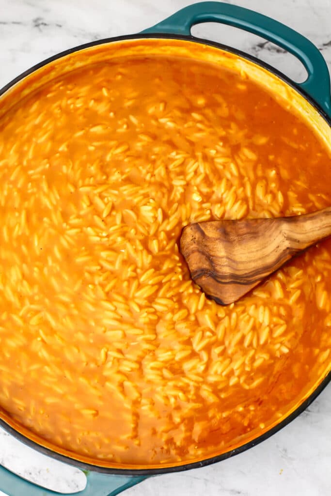 Creamy pumpkin risotto cooking in a large shallow blue skillet bein stirred with a wooden spoon.