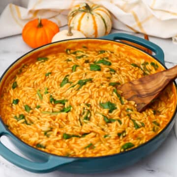 A large blue skillet filled with pumpkin orzo with spinach and little pumpkins in the background.
