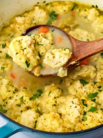 A pot of vegan chicken and dumplings being scooped up with a wooden ladle.