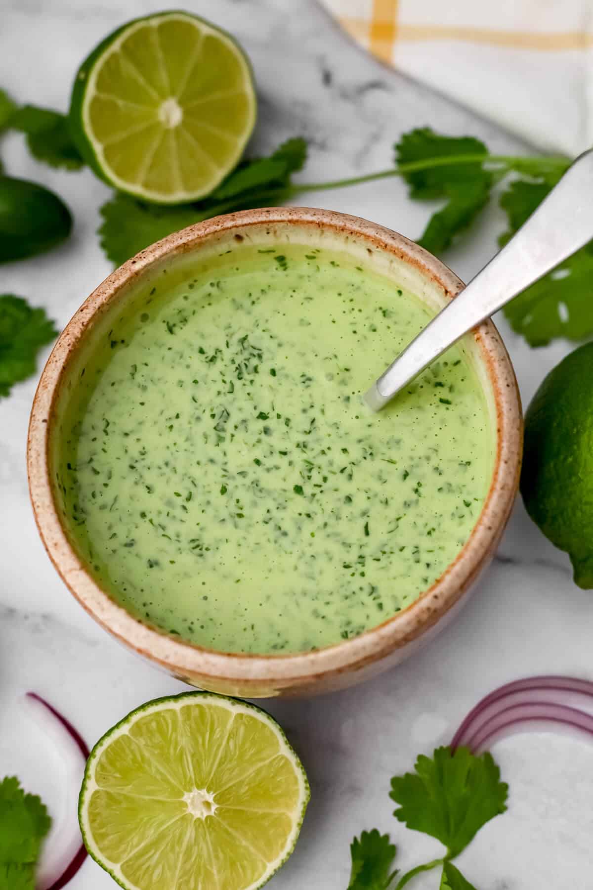 A top view of a bowl of vegan cilantro lime crema with cilantro and limes on the side.