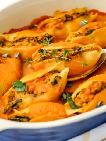 A blue casserole dish filled with vegan pumpkin stuffed shells with vegan pumpkin alfredo on top.