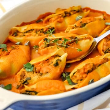 A blue casserole dish filled with vegan pumpkin stuffed shells with vegan pumpkin alfredo on top.