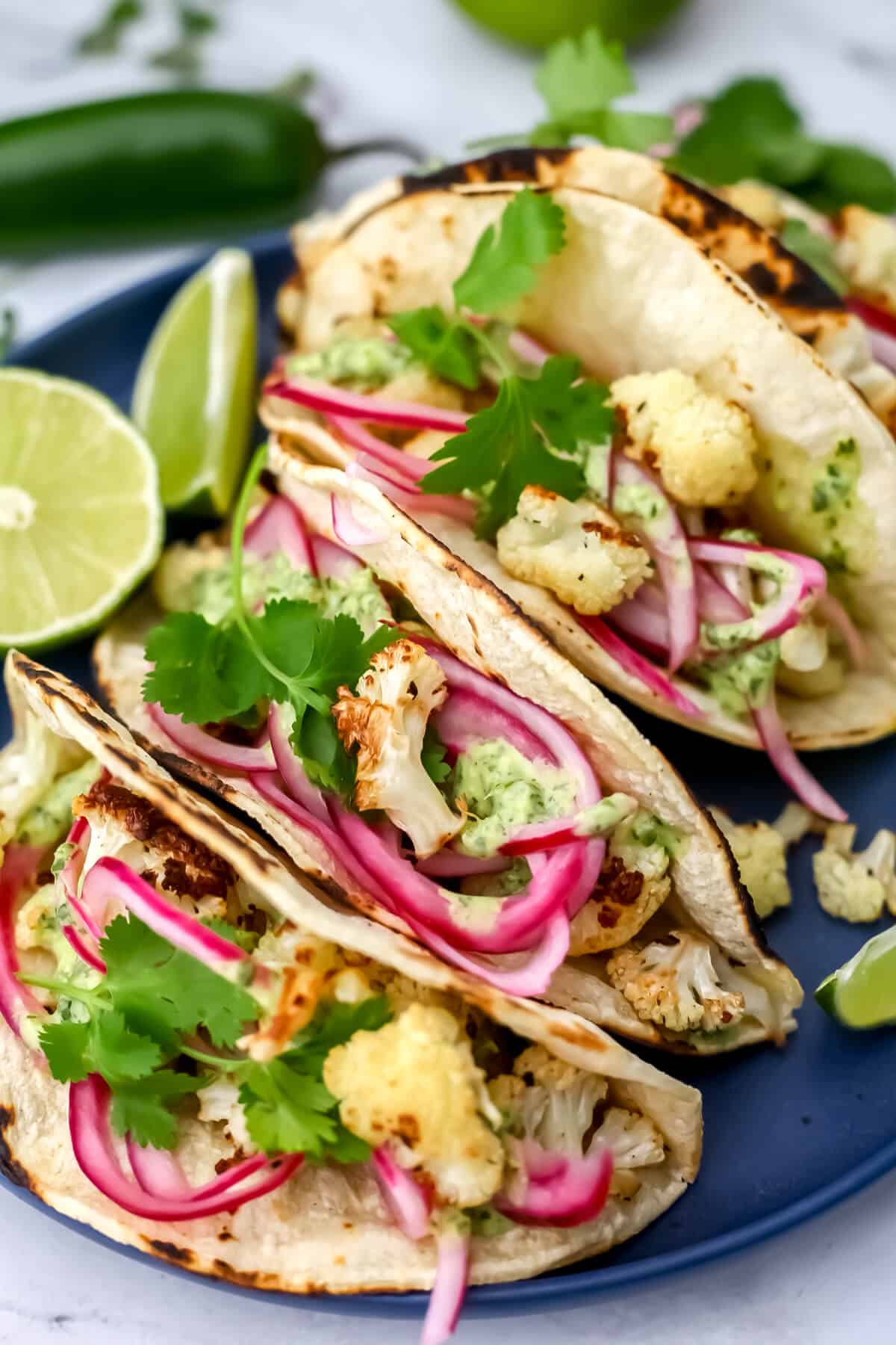 Cauliflower tacos on a blue plate with cilantro, Mexican pickled onions, and lime wedges around them.