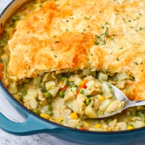 A vegan chicken pot pie made in a skillet with a pastry puff top with a spoon in it.