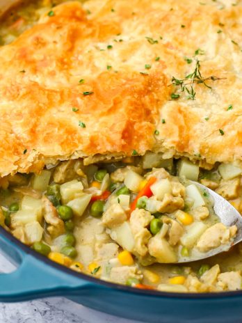 A vegan chicken pot pie made in a skillet with a pastry puff top with a spoon in it.
