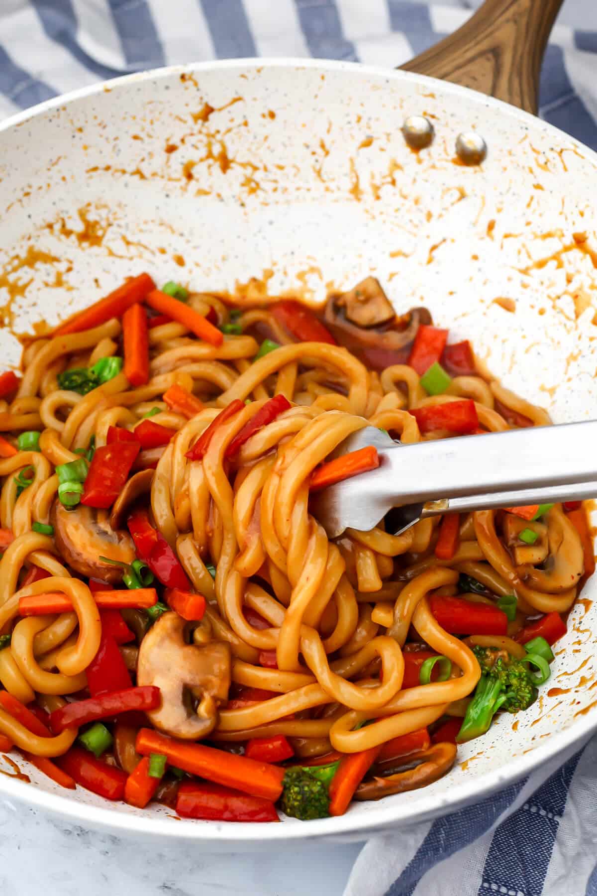 Vegan yaki udon noodles mixed with sauteed vegetables and stir-fry sauce in a white wok.