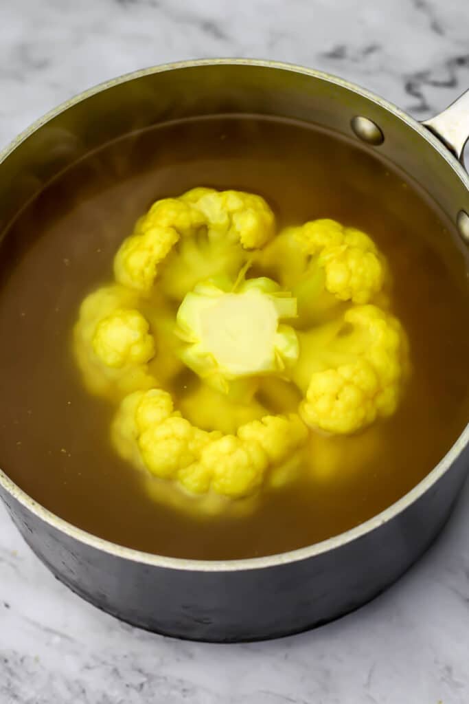 A whole head of cauliflower boiling in broth.