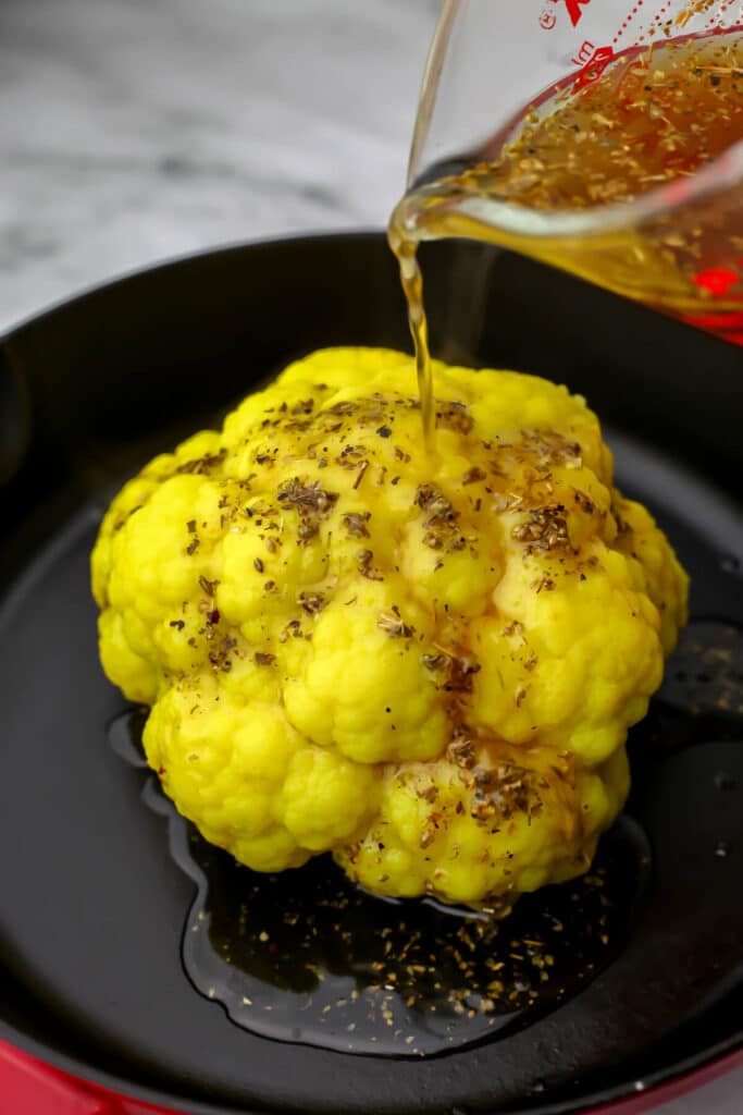 Pouring the basting liquid over the whole head of cauliflower.